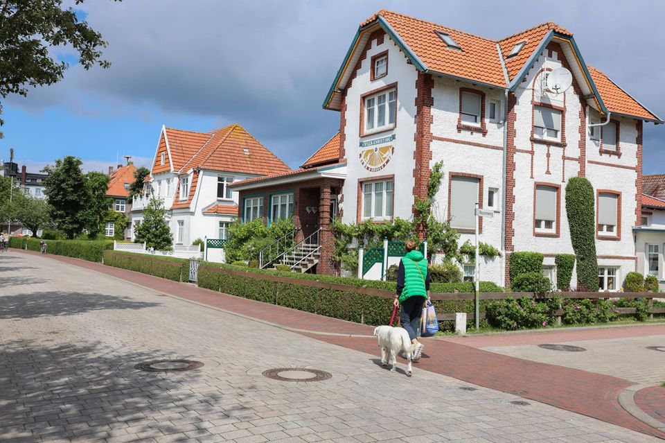 Eine Frau mit Hund geht die Bahnhofstrape auf Langeoog entlang