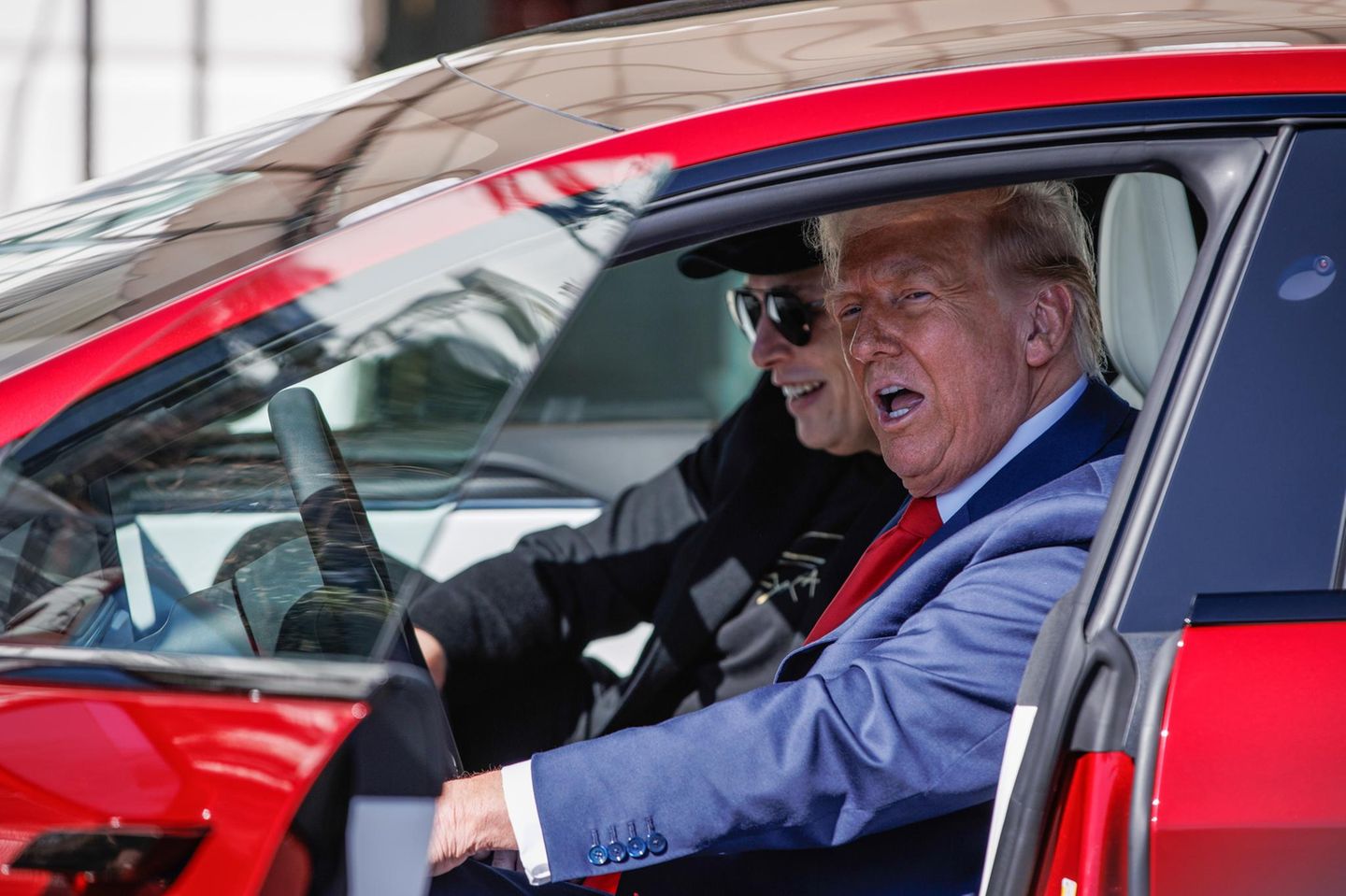 Donald Trump sitzt neben Elon Musk in einem roten Tesla
