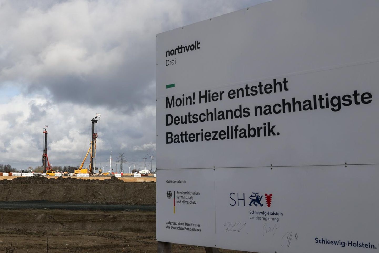Ein Bauschild mit dem Text „Moin! Hier entsteht Deutschlands nachhaltigste Batteriezellenfabrik“ steht an der Baustelle in Heide