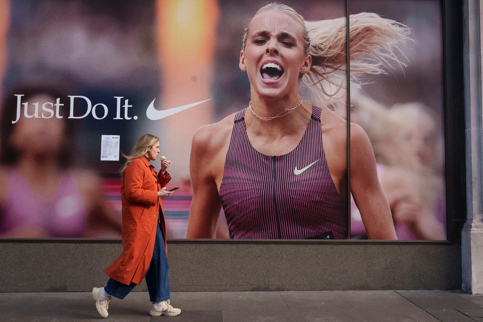 Eine Kundin isst und geht an einem „Just Do It“-Werbeslogan von Nike vorbei