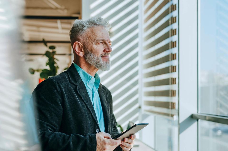 Geschäftsmann hält ein digitales Tablet und schaut aus dem Fenster in einem Büromodell