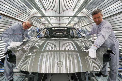 Zwei Porsche-Mitarbeiter prüfen in der Lackiererei den Lack der Karosserie eines vollelektrischen Porsche Macan
