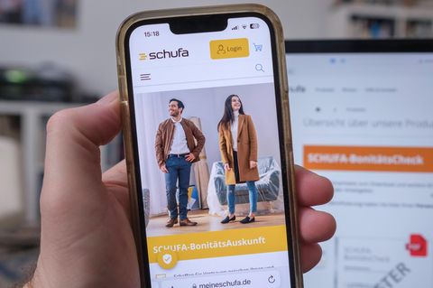 Mobiltelefon in einer Hand mit der Website der Schufa
