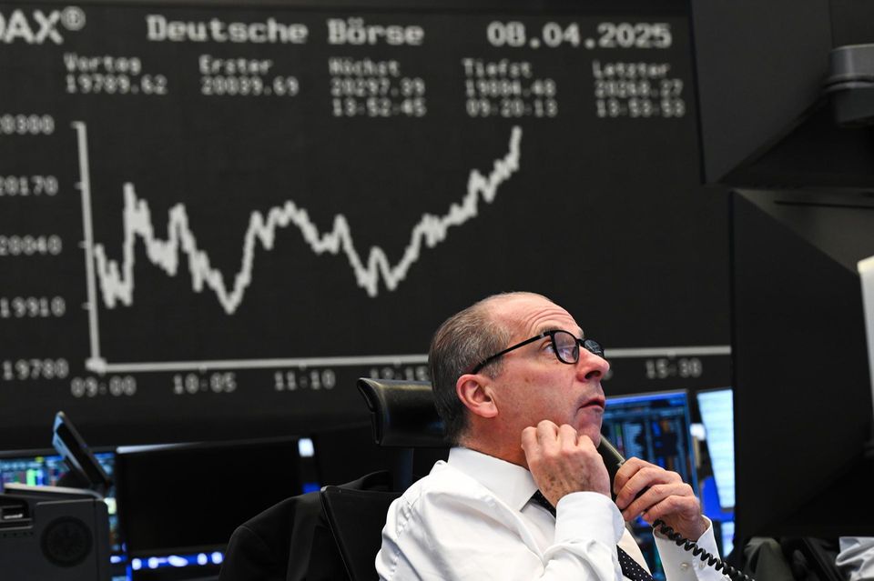 Ein Börsenhändler beobachtet vor der Anzeigetafel mit der Dax-Kurve seine Monitore