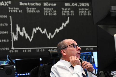 Ein Börsenhändler beobachtet vor der Anzeigetafel mit der Dax-Kurve seine Monitore