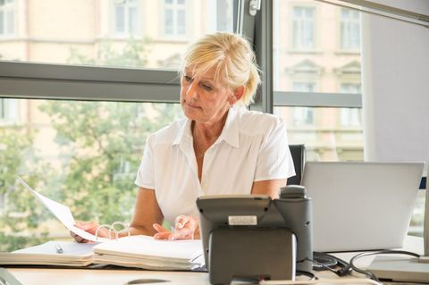 Eine Frau in Rente sitzt in einem Büro und ließt in einem Ordner