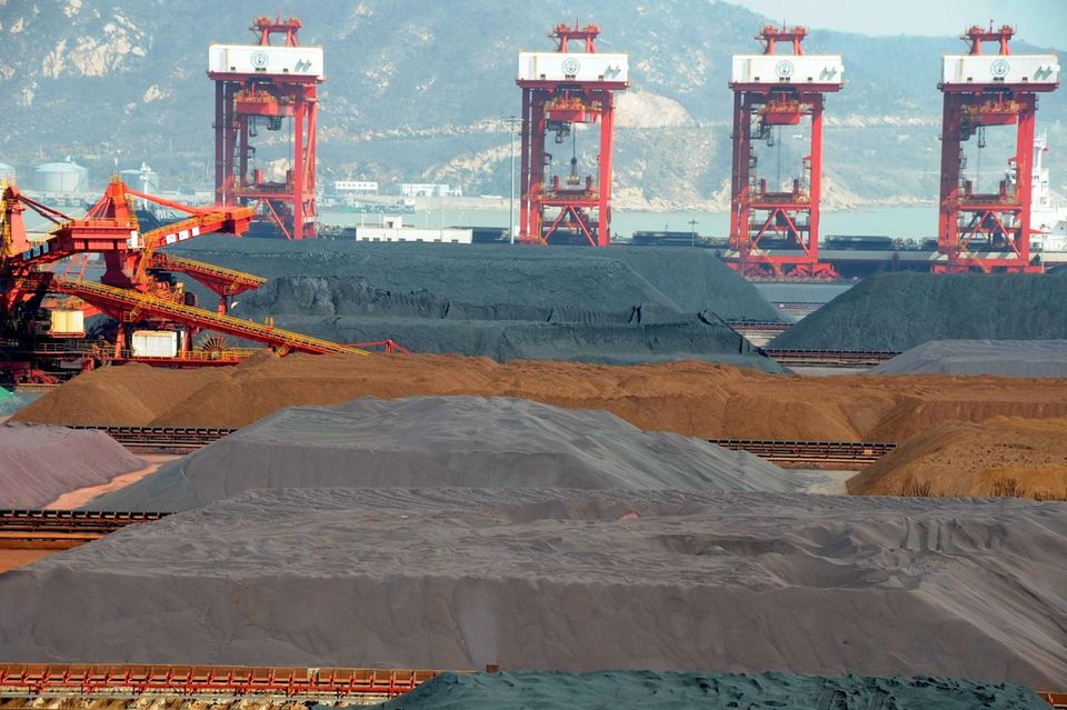 Eine Rohstoff-Mine in China, im Hintergrund beladen Kräne ein Frachtschiff