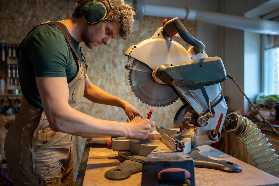Tischler benutzt Gehrungssäge, misst und schneidet Holzbalken in der Werkstatt zu