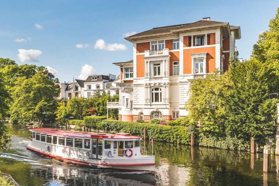 Ein Ausflugsschiff fährt auf der Alster an einer Villa