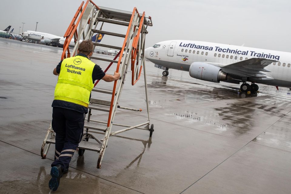 Ein Fluggerätmechaniker schiebt auf dem Rollfeld eine Treppe zu einem Flugzeug