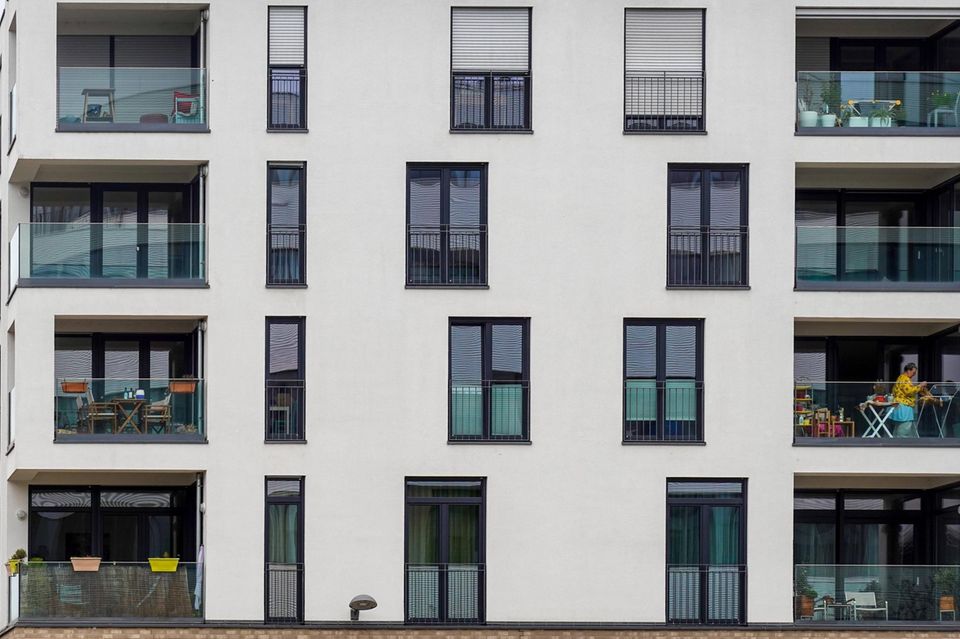 Eine Frau hängt Wäsche auf dem Balkon eines modernen Wohnhauses auf