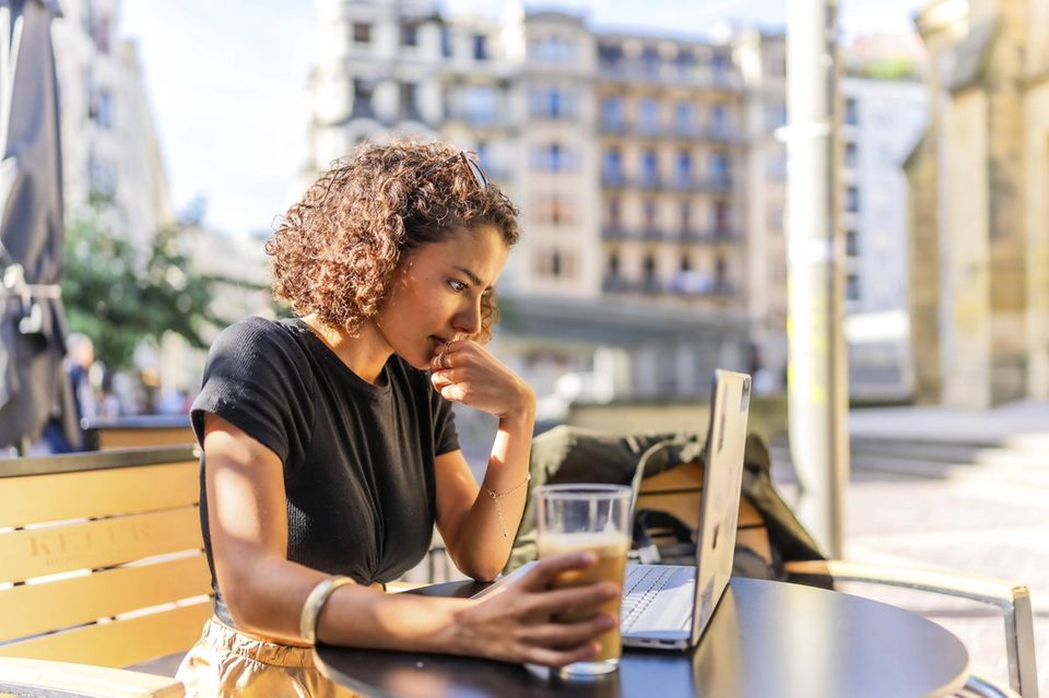 Geschäftsfrau trinkt Kaffee auf einer Terrasse und arbeitet mit einem Laptop