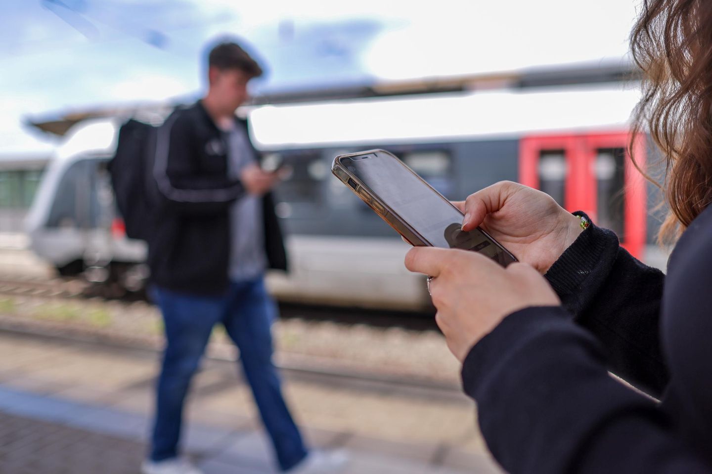 Eine Frau steht am Gleis und bedient die Bahn-App „DB Navigator“