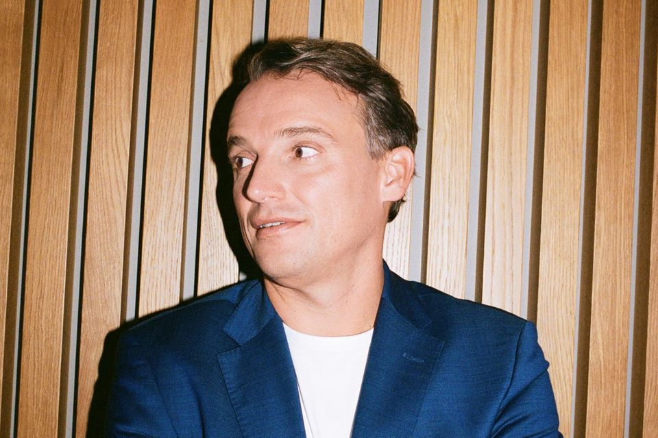 Christian Klein steht mit verschränkten Armen vor einer Wand