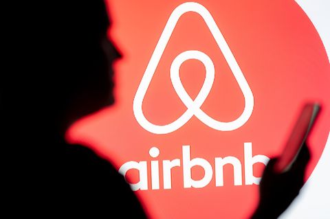 Eine Frau schaut auf ihr Smartphone, im Hintergrund ist das Airbnb-Logo zu sehen