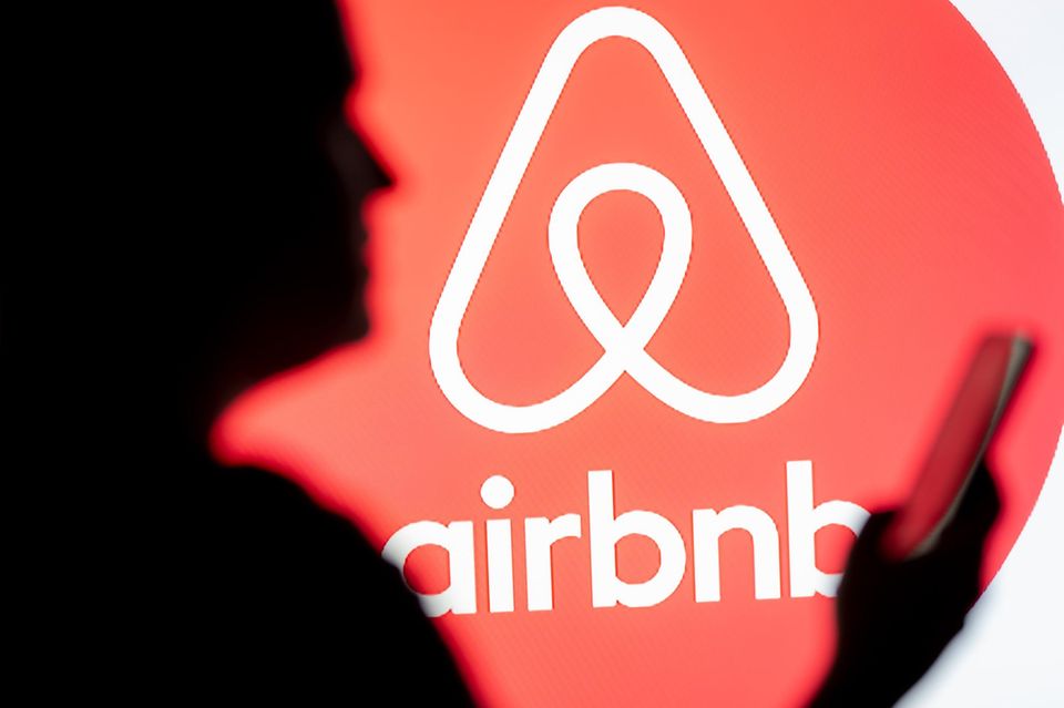 Eine Frau schaut auf ihr Smartphone, im Hintergrund ist das Airbnb-Logo zu sehen