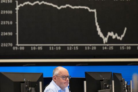 Ein Aktienhändler an der Börse schaut vor der Dax-Kurve auf einen Bildschirm