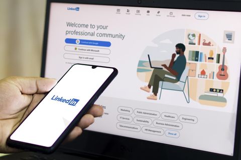 Auf einem Handybildschirm ist ein Linkedin-Logo, auf eine Laptop dahinter die Linkedin-Startseite