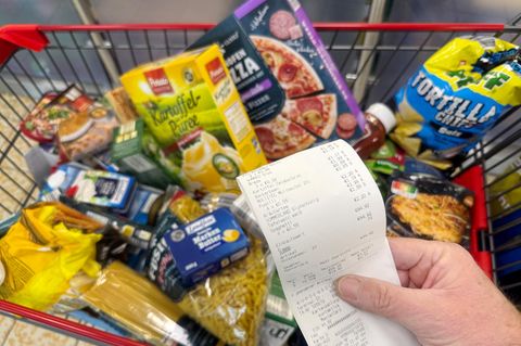 Eine Supermarktrechnung zeigt die Preise, dahinter ein voller Einkaufswagen