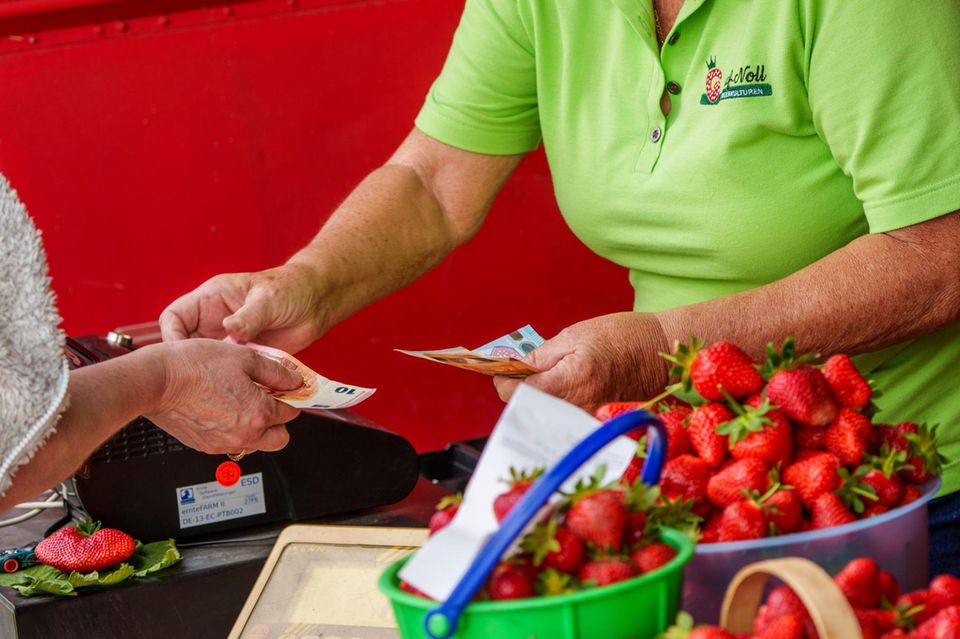 Eine Person bezahlt an der Kasse selbstgepflückte Erdbeeren