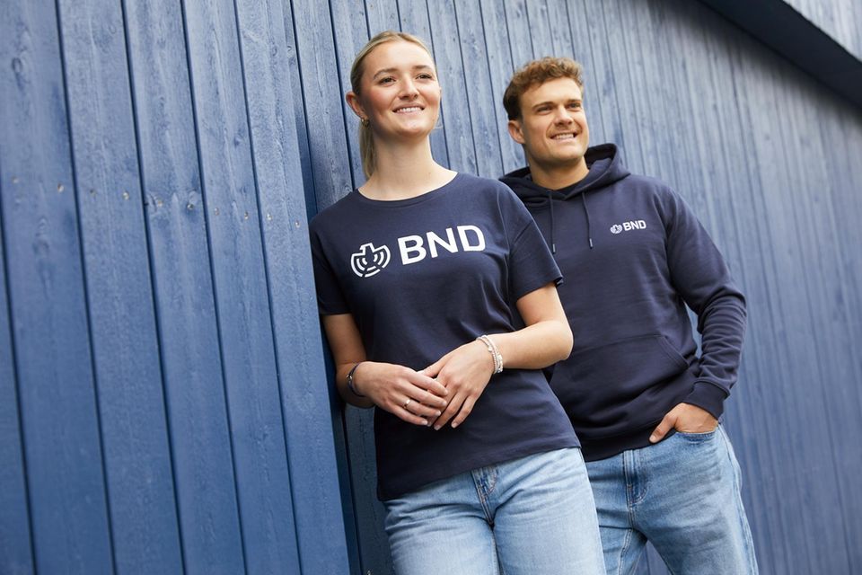 In einem Werbefoto trägt eine Frau ein BND-Shirt, ein Mann einen BND-Hoodie