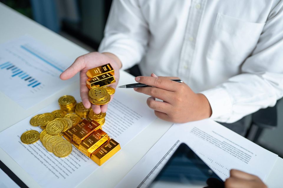 Person hält Goldbarren und Goldmünzen