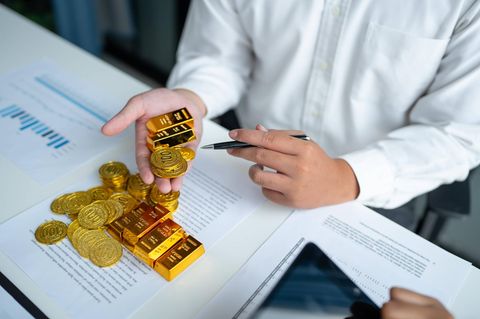 Person hält Goldbarren und Goldmünzen