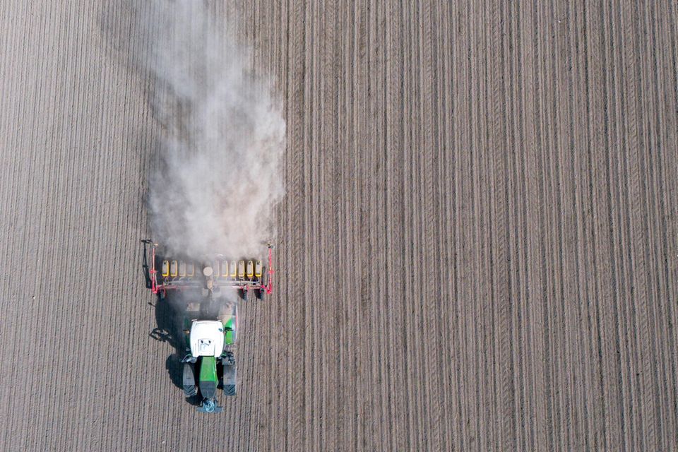 Ein Traktor fährt über ein Feld und zieht eine Staubwolke hinter sich her