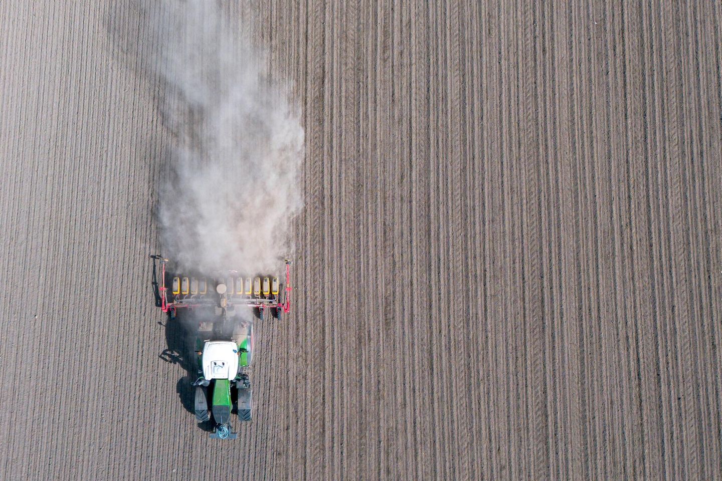 Ein Traktor fährt über ein Feld und zieht eine Staubwolke hinter sich her