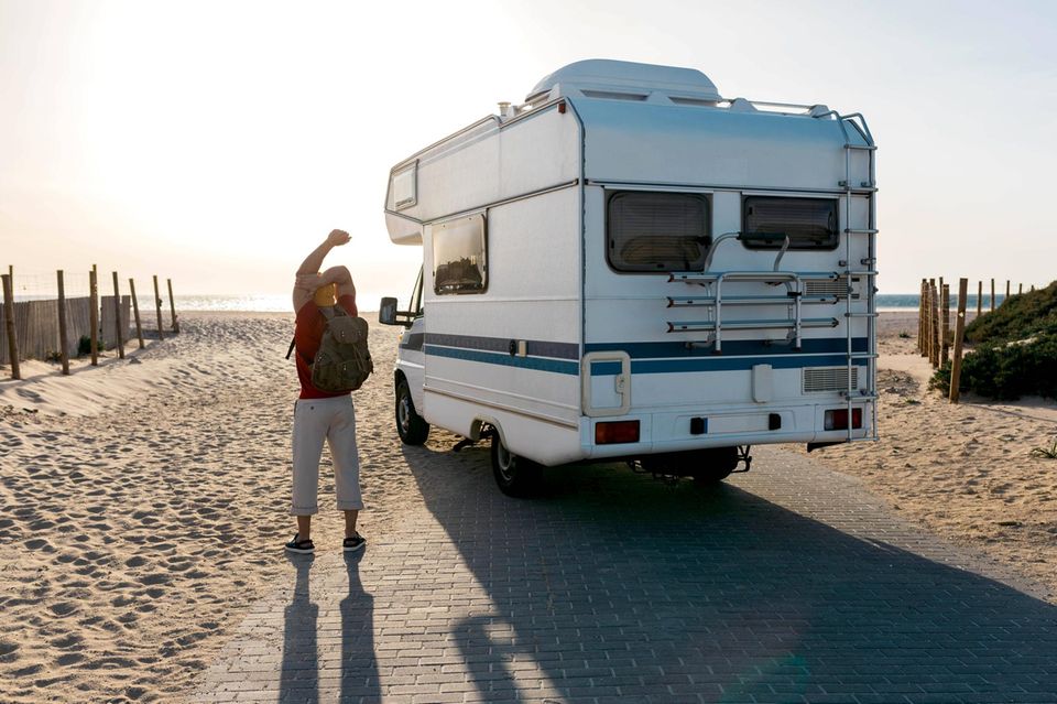 Urlaub: Mann neben Wohnmobil am Strand