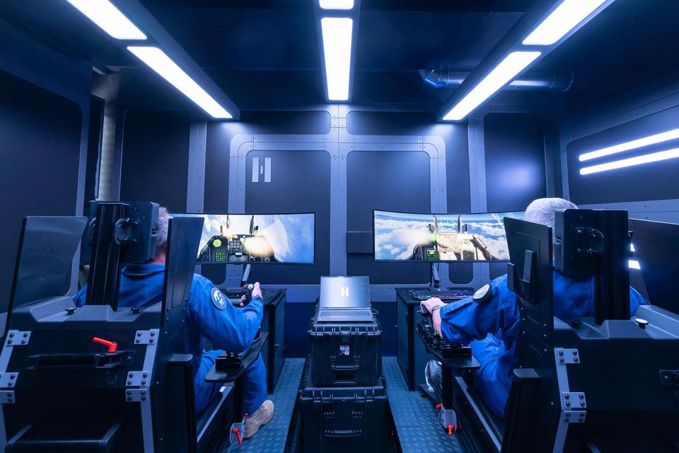 Dos pilotos de combate de Helsing se sientan en el simulador de vuelo en una sala de diseño futurista.