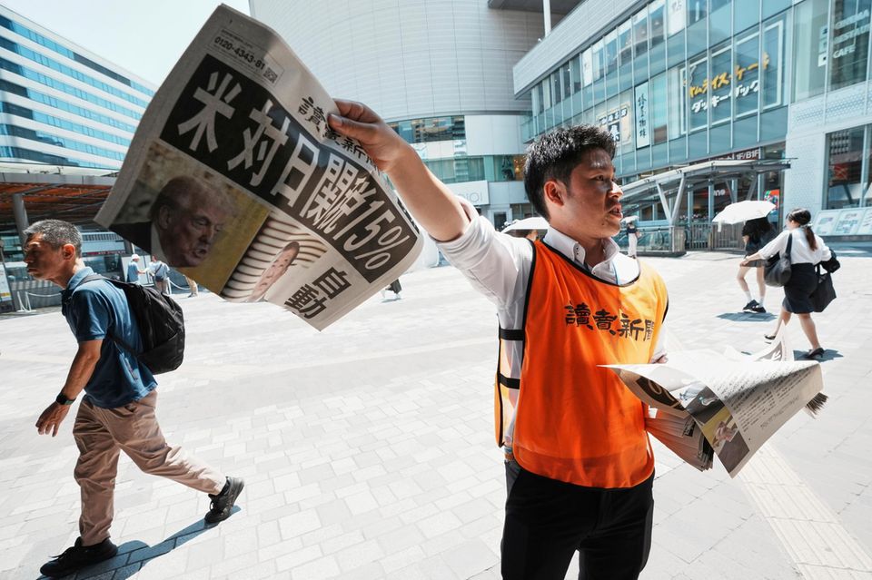 Ein Zeitungsverkäufer mit einem Titelblatt zum Handels-Deal zwischen USA und Japan
