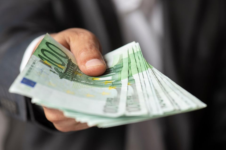 Salário em dinheiro do chefe: Um homem entrega ao espectador um punhado de notas de 100 euros