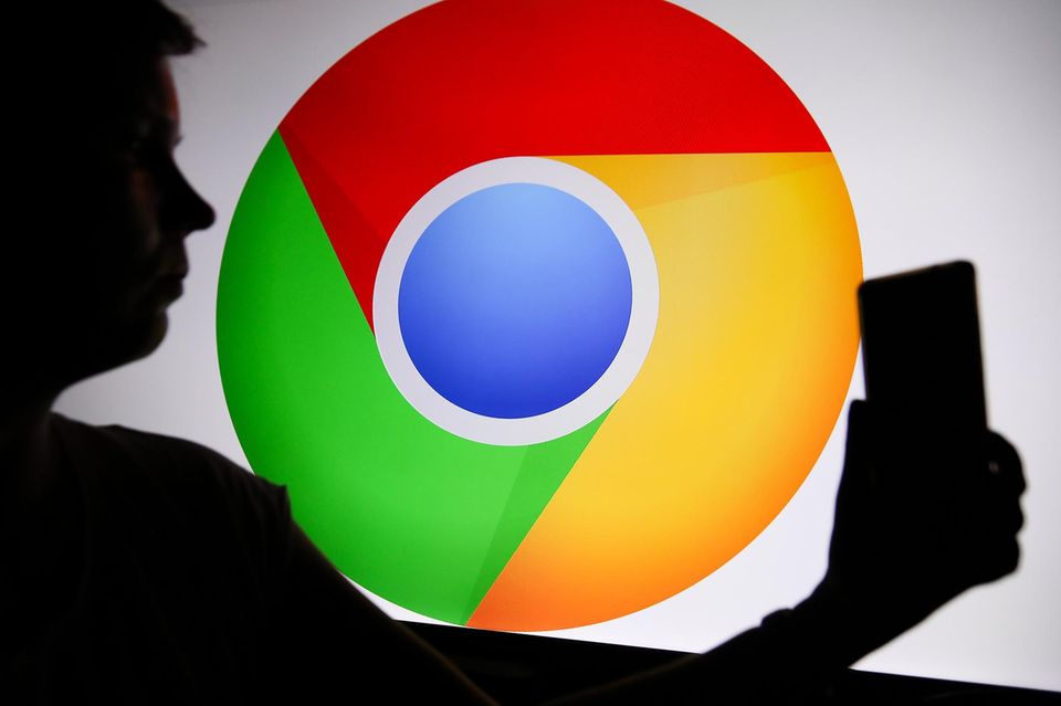 Das Chrome-Logo ist zu sehen, während eine Person ein Telefon in der Hand hält