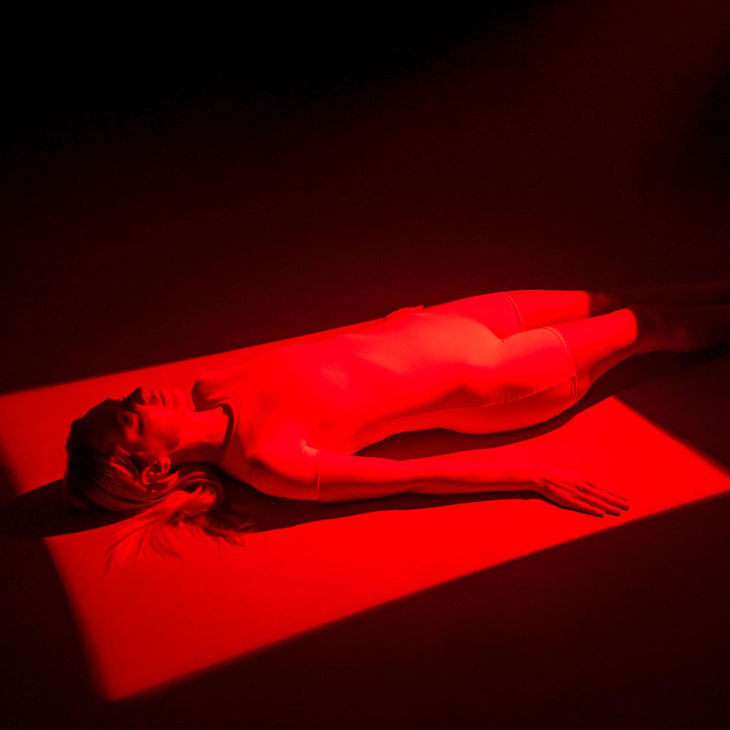 Eine in rotes Licht getauchte Frau liegt auf einer Liege