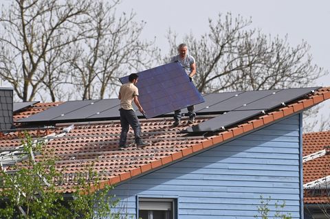 Zwei Handwerker montieren eine Photovoltaik-Anlage auf einem Hausdach