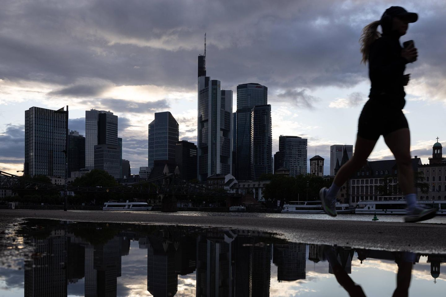 ine Joggerin läuft bei Regen vor der Frankfurter Bankenskyline am Mainufer entlang