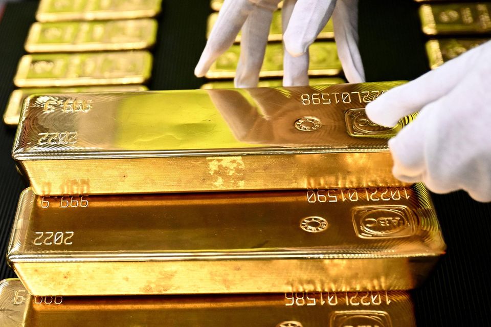 Eine Person mit weißen Handschuhen stapelt Goldbarren