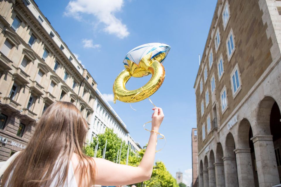 Frau hält Luftballon in Form eines Rings in die Luft