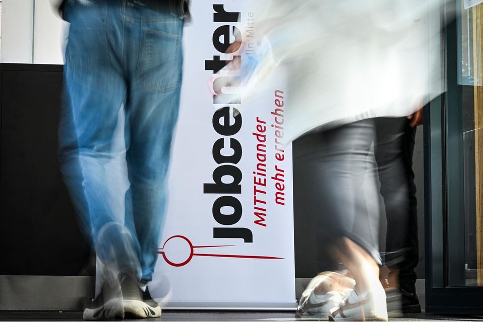Personen gehen am Logo vom Jobcenter Berlin-Mitte bei einer Jobmesse vorbei