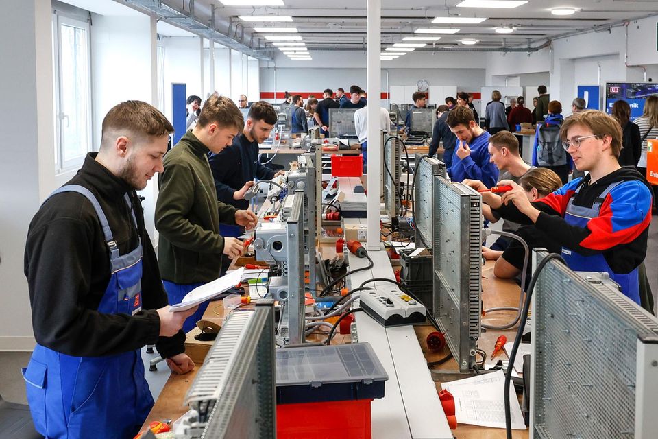 Gewerblich technisch Auszubildende stehen in einer Reihe und hantieren mit Kabeln