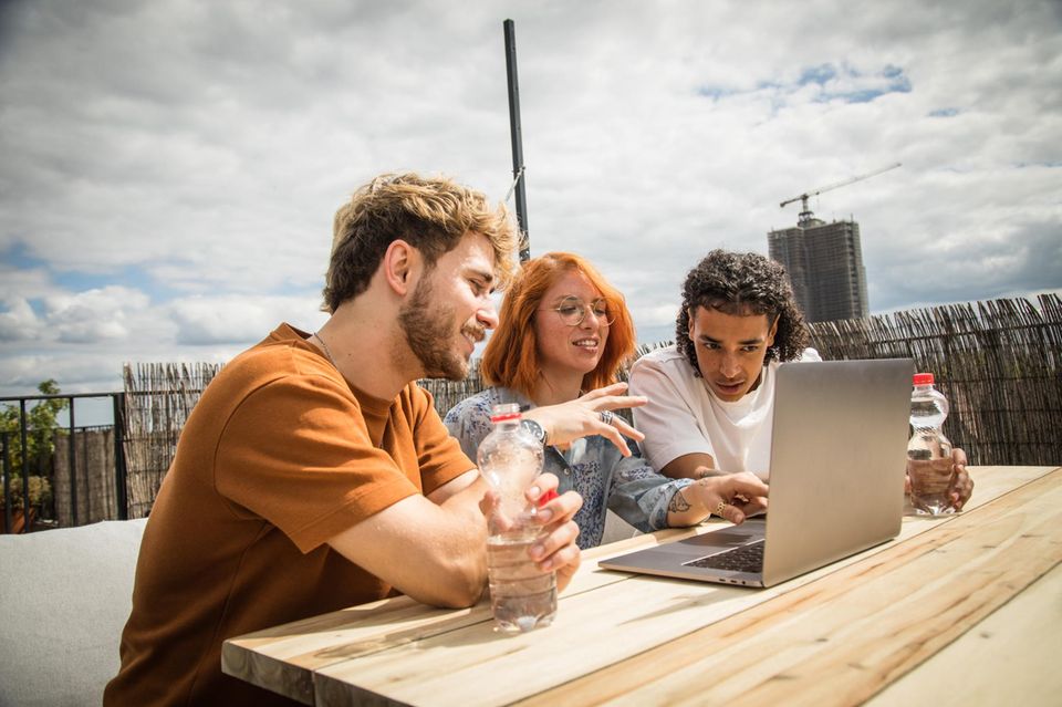 Studenten sitzen auf einer Dachterasse und schauen in einen Laptop