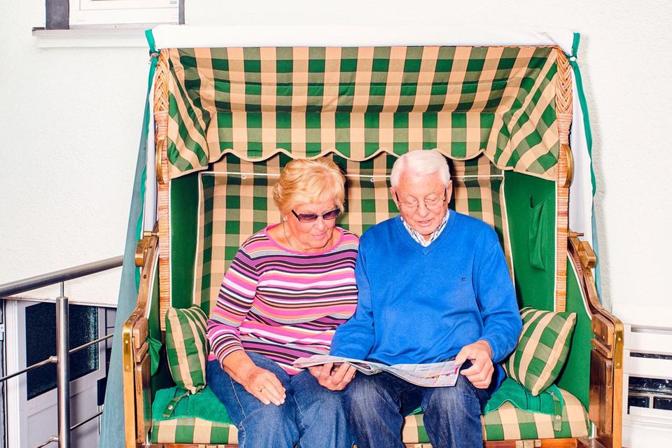Zwei Senioren sitzen in einem Strandkorb vor einem Haus
