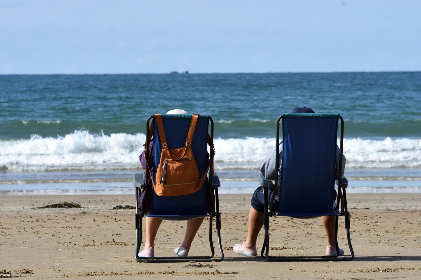 Ehepaar sitzt in Campingstuehlen am Strand und schaut aufs Meer Ehepaar sitzt in Campingstuehlen am Strand und schaut aufs Meer