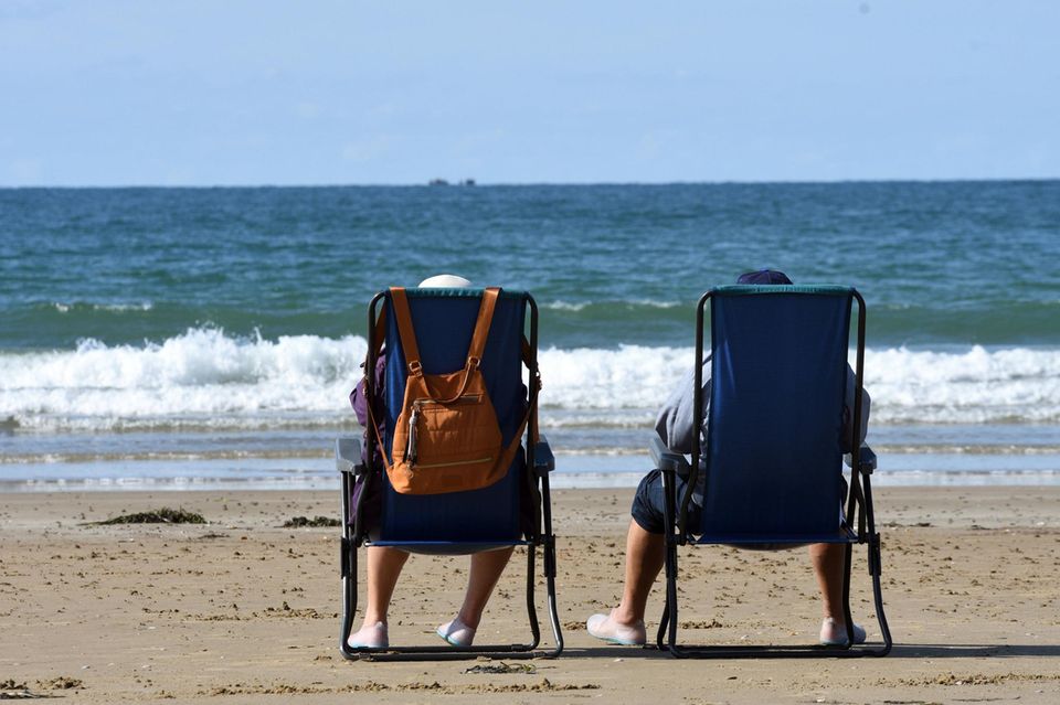Ehepaar sitzt in Campingstuehlen am Strand und schaut aufs Meer Ehepaar sitzt in Campingstuehlen am Strand und schaut aufs Meer