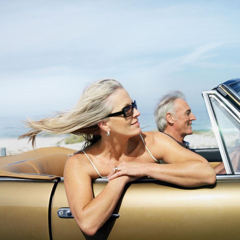 Eine Frau und ein Mann brausen im Cabrio am Meer entlang