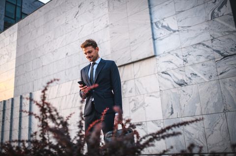 Ein junger Mann mit Aktentasche in der Hand blickt auf sein Handy.