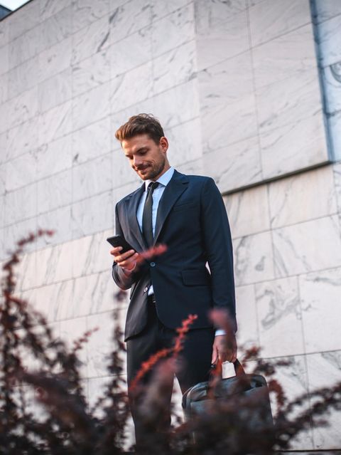 Ein junger Mann mit Aktentasche in der Hand blickt auf sein Handy.