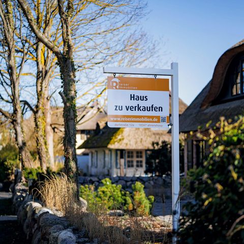 Ein Schild mit der Aufschrift  Haus zu verkaufen  steht vor einem mit Reet gedecktem Haus im Ostseebad Ahrenshoop