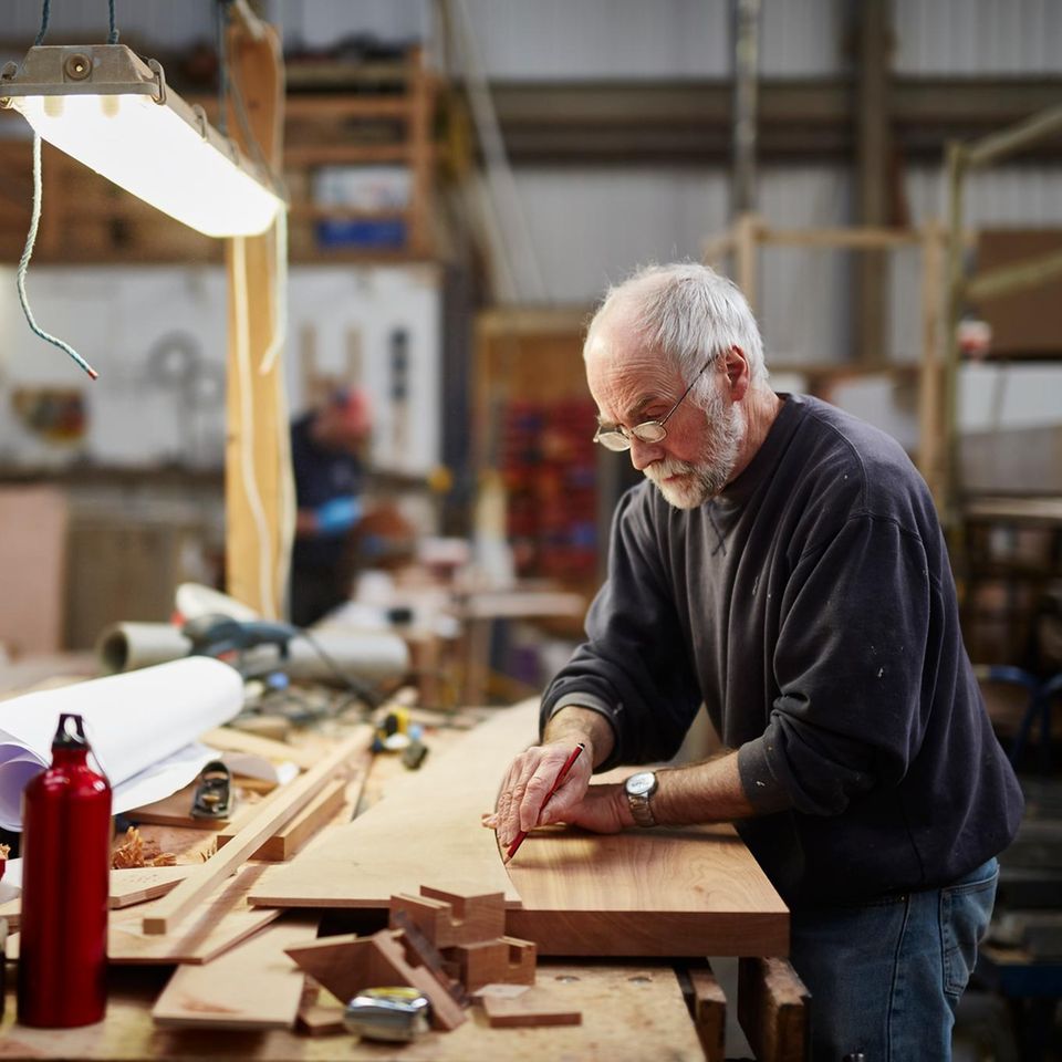 Handwerker in fortgeschrittenem Alter bereitet eine Holzplatte fürs Zuschneiden vor: Rente mit 70 Symbolbild